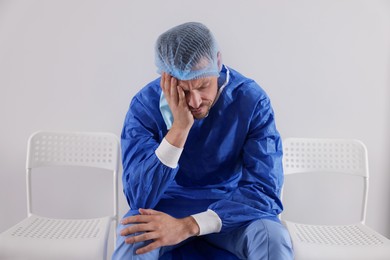 Exhausted doctor sitting on chair near grey wall