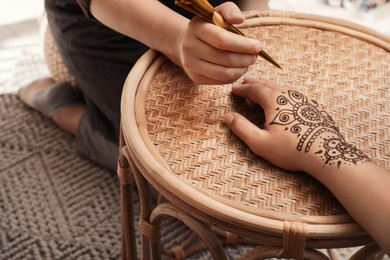 Master making henna tattoo on hand at table, closeup. Traditional mehndi