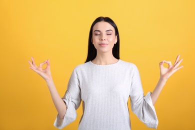 Young woman meditating on yellow background. Stress relief exercise
