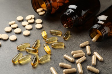 Photo of Overturned bottles with different dietary supplements on grey table, closeup