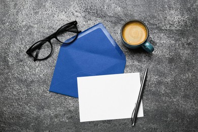 Envelope with blank paper card, cup of coffee, pen and glasses on grey table, flat lay