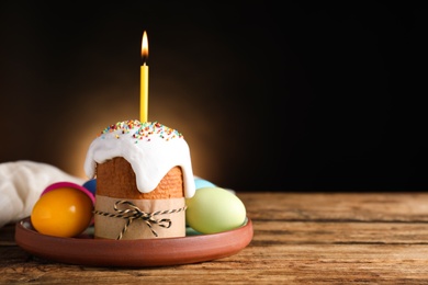 Traditional Easter cake with burning candle on wooden table against black background. Space for text