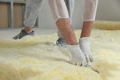 Worker cutting insulation material indoors, closeup. Space for text