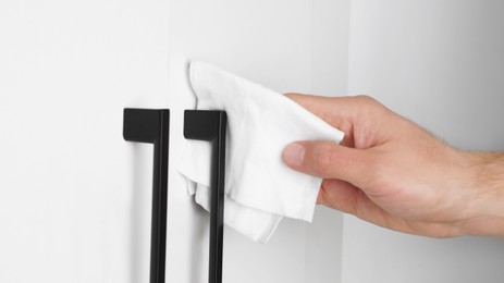 Photo of Man cleaning wardrobe handle with disinfecting wipe indoors, closeup. Protective measures