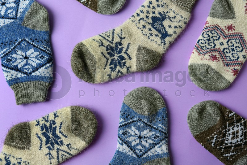 Different knitted socks on violet background, flat lay. Winter clothes