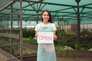 Photo of Female business owner holding OPEN sign in greenhouse