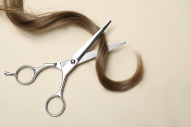 Professional hairdresser scissors and hair strand on beige background, flat lay. Haircut tool