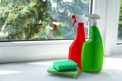 Spray bottles of detergents and sponges on window sill indoors, space for text. Cleaning supplies