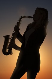 Silhouette of woman playing saxophone against beautiful sky at sunset