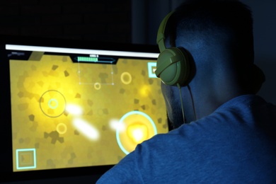 Man with headphones playing video game on modern computer in dark room