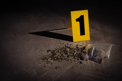 Scattered cannabis and crime scene marker on grey stone table. Space for text