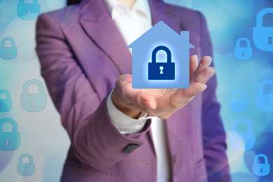 Home security concept. Woman holding house on light background, closeup