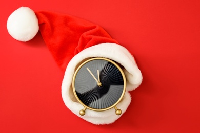 Alarm clock with Santa hat on red background, top view. New Year countdown