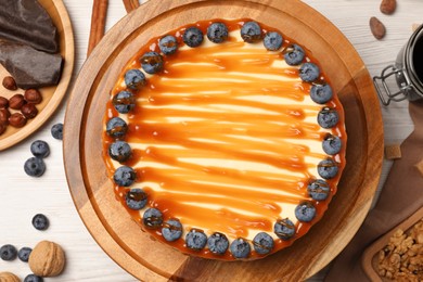 Photo of Delicious cheesecake with caramel and blueberries on white wooden table, flat lay