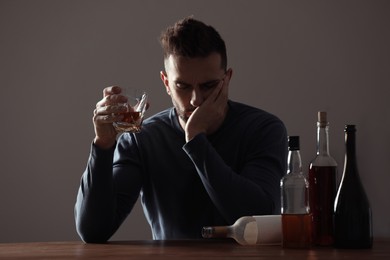 Addicted man with alcoholic drink at wooden table indoors