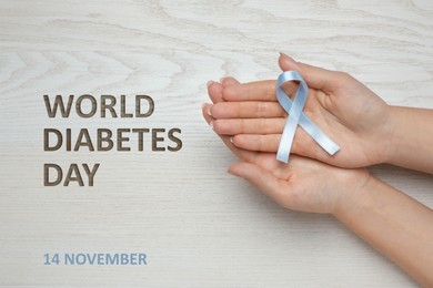 World Diabetes Day. Woman with light blue awareness ribbon at wooden table, closeup