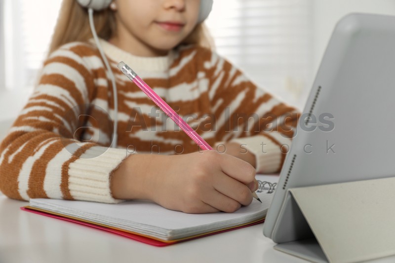 Photo of Cute little girl with modern tablet studying online at home, closeup. E-learning