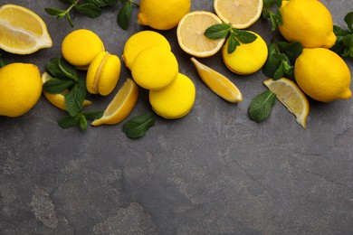 Delicious yellow macarons, fresh lemons and mint on grey table, flat lay. Space for text