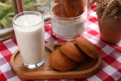 Glass of milk with cookies on red checkered tablecloth indoors