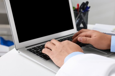 Photo of Doctor working with laptop at white desk in clinic, closeup. Online medicine