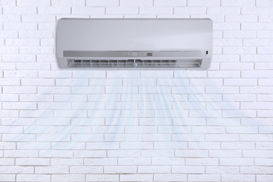Modern air conditioner on white brick wall indoors