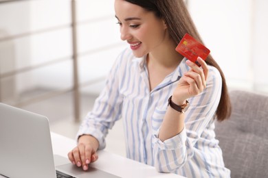 Woman with credit card using laptop for online shopping at white table indoors, closeup