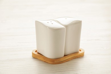Photo of Ceramic salt and pepper shakers with stand on white wooden table, closeup