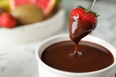 Dipping strawberry into fondue pot with chocolate, closeup. Space for text