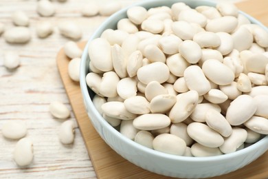 Bowl with uncooked white beans on wooden table, closeup
