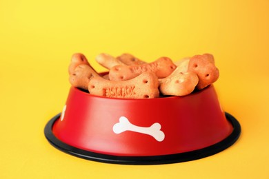 Photo of Bone shaped dog cookies in feeding bowl on yellow background