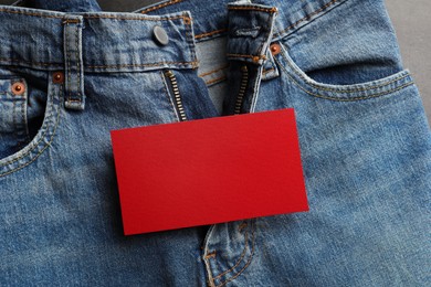 Photo of Blue jeans with unbuttoned fly and red blank card on grey background, top view. Exhibitionist concept
