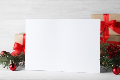 Blank greeting card near Christmas decorations on white table, closeup. Space for text