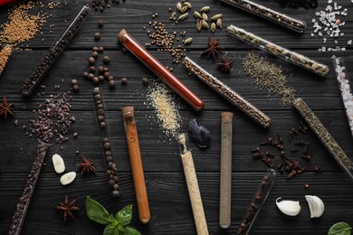 Flat lay composition with various spices, test tubes and fresh herbs on black wooden background