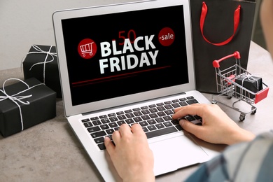 Woman using laptop with Black Friday announcement at grey table, closeup