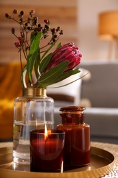 Photo of Vase with beautiful protea flower and candles on wicker stand indoors. Interior elements