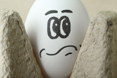 Egg with drawn thoughtful face in cardboard package, closeup