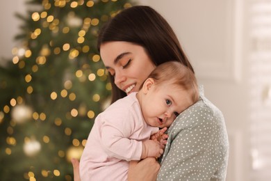 Happy young mother with her cute baby against blurred festive lights. Winter holiday
