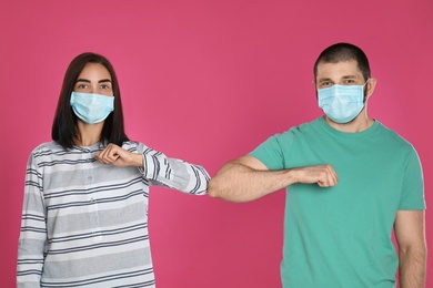 Man and woman bumping elbows to say hello on pink background. Keeping social distance during coronavirus pandemic