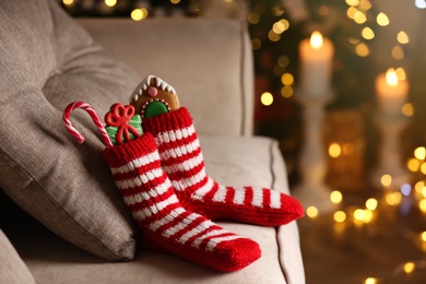 Socks filled with sweets on sofa in room, space for text. Saint Nicholas Day