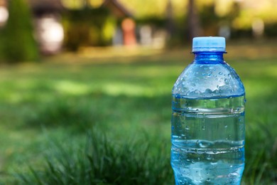 Photo of Plastic bottle of water on green grass outdoors, closeup. Space for text