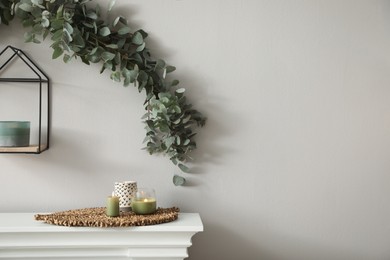 Beautiful garland made of eucalyptus branches and aromatic candle hanging above mantelpiece indoors
