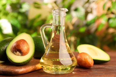 Photo of Fresh avocados and jug of cooking oil on wooden table against blurred green background, closeup