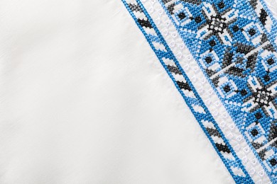 Photo of Beautiful light blue Ukrainian national embroidery on white fabric, top view. Space for text