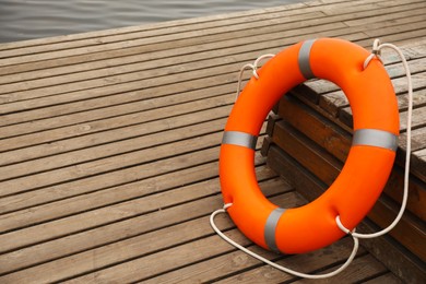 Orange lifebuoy on wooden pier, space for text. Rescue equipment