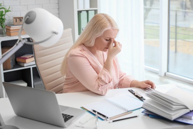 Mature woman suffering from headache while sitting at table in office