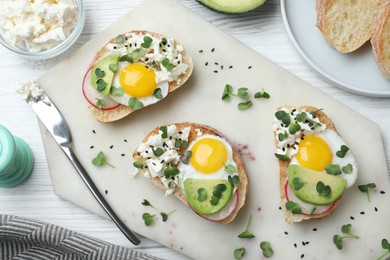 Delicious sandwiches with egg, cheese, avocado and microgreens on white wooden table, flat lay