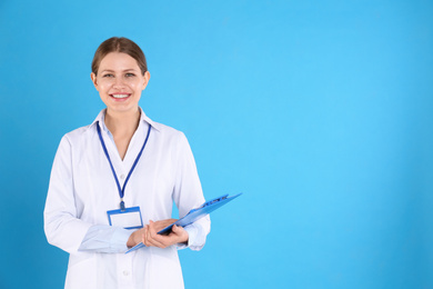 Portrait of young doctor with clipboard on blue background, space for text