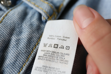 Woman reading clothing label with care symbols and material content on jeans, closeup