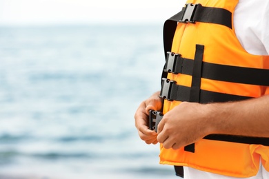 Male lifeguard putting on life vest near sea, closeup