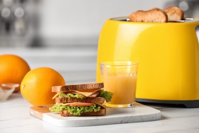 Yellow toaster with roasted bread slices, sandwich, oranges and juice on white marble table